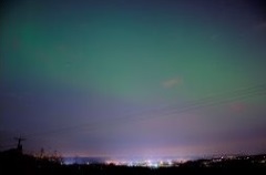 This picture shows a green turquise aurora curtain hovering way above the town of Wellington with the shining street lights below